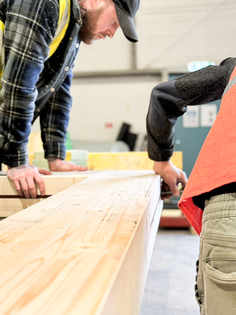 Two men work on inserting a piece of steel into a precision cut slot in a piece of timber.