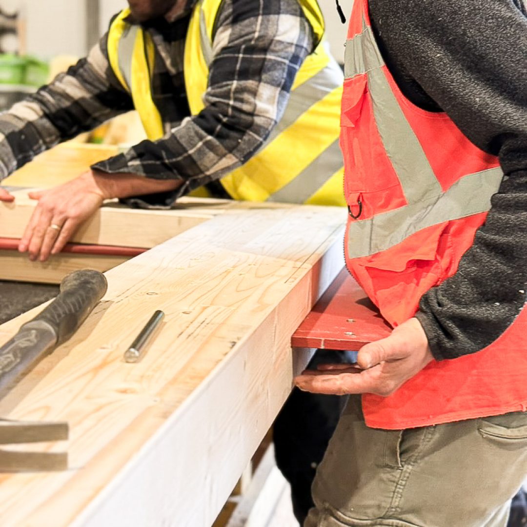 Two men work on inserting a piece of steel into a precision cut slot in a piece of timber.